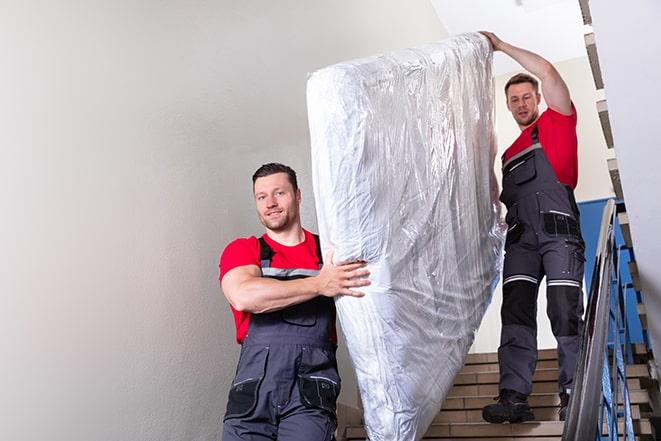 two people carrying a box spring out of a bedroom in Clay